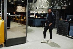 Handsome african american man posing  inside night club in black hat. photo