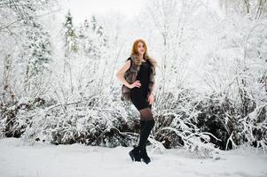 Red haired girl in fur coat walking at winter snowy park. photo