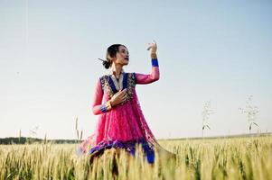 tierna niña india en sari, con maquillaje de labios violetas posada en el campo al atardecer. modelo indio de moda. foto