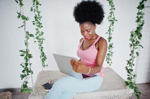 Young african american woman sitting in bed while working on laptop and listen music on earphones. photo