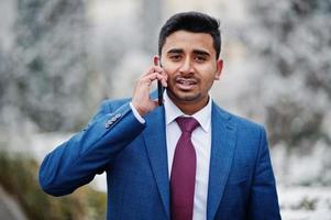 elegante modelo indio de moda en traje posado en el día de invierno y hablando por teléfono. foto