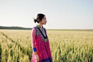 tierna niña india en sari, con maquillaje de labios violetas posada en el campo al atardecer. modelo indio de moda. foto