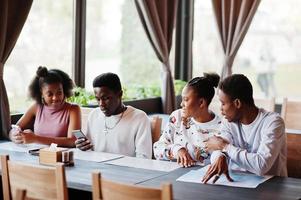 felices amigos africanos sentados y charlando en el café. grupo de personas negras reunidas en un restaurante y miran su teléfono móvil. foto