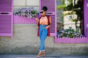 African american girl in sunglasses posed against purple windows with cell phone at hand. photo