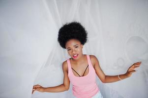 joven mujer afroamericana en camiseta rosa contra ventana tocando tul. mañana perfecta. foto