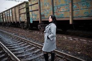 chica morena con abrigo gris posada en la estación de tren. foto