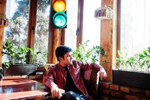 Stylish indian man in casual wear sitting indoor cafe against traffic light. photo