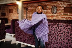 African woman in checkered violet cape posed at cafe. photo