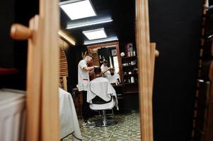 un joven barbudo que se corta el pelo con un peluquero mientras se sienta en una silla en la barbería. alma de barbero. foto