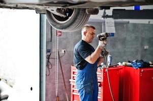 Car repair and maintenance theme. Mechanic in uniform working in auto service. photo