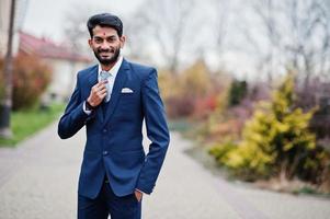 hombre indio de barba elegante con bindi en la frente, vestido con traje azul posado al aire libre. foto