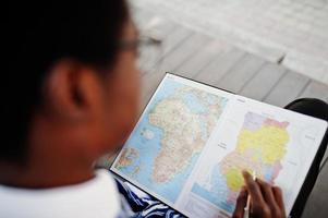 African man in traditional clothes and glasses looking on map of Africa and Ghana at his notebook. photo