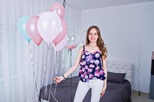 Happy girl with colored balloons on bed at room. Celebrating birthday theme. photo