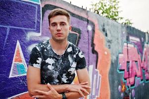 retrato de estilo de vida de un hombre guapo posando en la calle de la ciudad con una pared de graffiti. foto