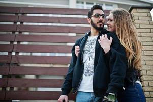 Cool multiracial couple hugs together against wooden fence. photo