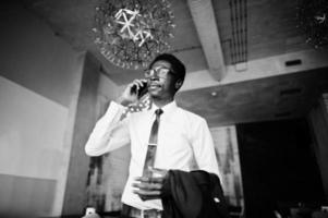 Business african american man wear on white shirt, tie and glasses at office speaking on mobile phone. photo