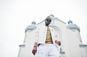 African american man in hat and sunglasses stand against church. Faith and Christianity in Africa. photo