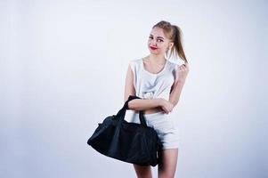 Amazing fit sexy body brunette caucasian girl posing at studio against white background on shorts and top with black sport bag. photo