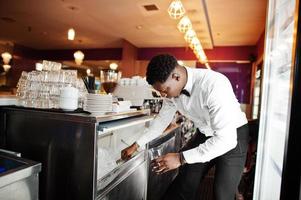 African american bartender at bar picks up ice. Alcoholic beverage preparation. photo