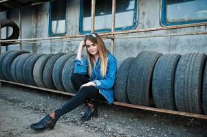 Young hipster girl in jeans jacket and head scarf at tire fitting zone. photo