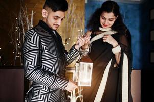 Lovely indian couple in love, wear at saree and elegant suit, posed on restaurant and hold lantern together. photo