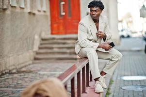 Stylish afro man in beige old school suit with mobile phone at hand. Fashionable young African male in casual jacket on bare torso. photo