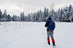 Back of man tourist with backpack. walking at pine trees covered by snow. Beautiful winter landscapes. Frost nature. photo