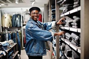 Stylish casual african american man at jeans jacket and black beret at clothes store looking on pants at shelves. photo