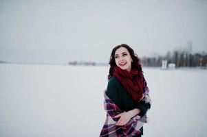 Brunette girl in green sweater and red scarf with plaid outdoor frozen lake on evening winter day. photo