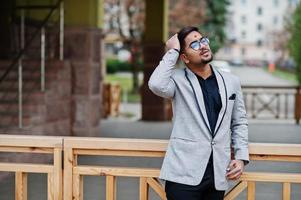 Stylish indian man with bindi on forehead and glasses, wear on gray suit posed outdoor. photo