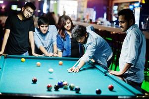 Group of stylish asian friends wear on jeans playing pool billiard on bar. photo