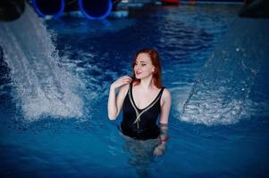 sexy chica pelirroja en traje de baño negro descansando en la piscina del parque acuático. foto