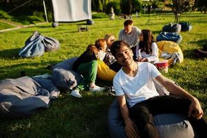 joven grupo multiétnico de personas viendo películas en poof en cine al aire libre. cierra el retrato de un tipo divertido. foto