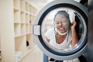 Funny portrait of cheerful african american woman near washing machine in the self-service laundry. photo