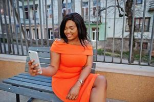 African american woman model xxl in orange dress looking on mobile phone. photo