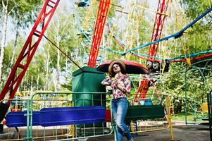 retrato de una chica morena con gafas rosas y sombrero con helado en el parque de atracciones. foto