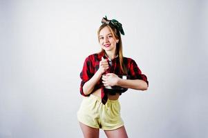 Young funny housewife in checkered shirt and yellow shorts pin up style with saucepan and kitchen spoon isolated on white background. photo