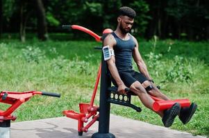 African american male athlete sport man with running sports arm case for mobile phone, doing exercises on the street workout simulators. photo