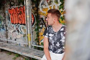 Lifestyle portrait of handsome man posing on the street of city with graffiti wall. photo