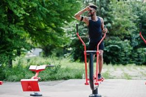 African american male athlete sport man with running sports arm case for mobile phone, doing exercises on the street workout simulators. photo