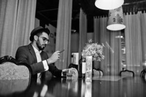 Handsome well-dressed arabian man with glass of whiskey and cigar posed at pub. photo