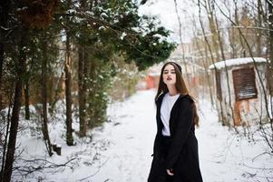 modelo morena de piernas largas de moda en capa negra larga y sombrero al aire libre en el día de invierno. foto