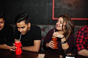 Group of indian friends having fun and rest at night club, drinking cocktails. photo