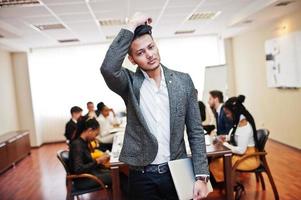 Face of handsome asian business man, holding laptop on the background of business peoples multiracial team meeting, sitting in office table. photo