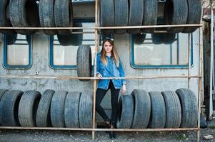 joven hipster con chaqueta de jeans y pañuelo en la cabeza en la zona de montaje de neumáticos. foto