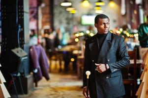 elegante caballero afroamericano con elegante chaqueta negra, sosteniendo un bastón retro como matraz de caña o bastón basculante con mango de bola de diamante dorado. rico hombre afro de moda. foto