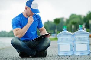 Delivery man sitting with clipboard water bottles outdoor. photo