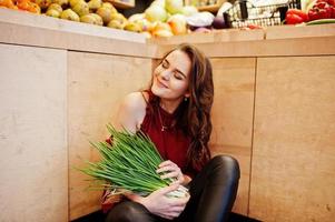 chica de rojo con cebollas verdes en la tienda de frutas. foto