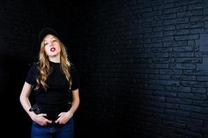 FBI female agent in cap and with gun at studio against dark brick wall. photo