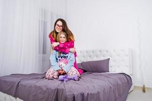 Two friends girls in pajamas having fun on bed at room. photo